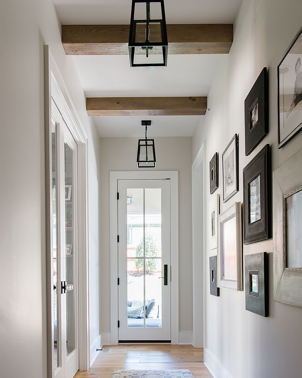 Hallway with white walls, wood beams, framed pictures, and black lantern lights.
