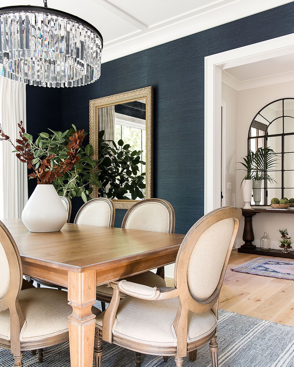 Dining room with wooden table, upholstered chairs, ornate mirror, and dark blue wallpaper.