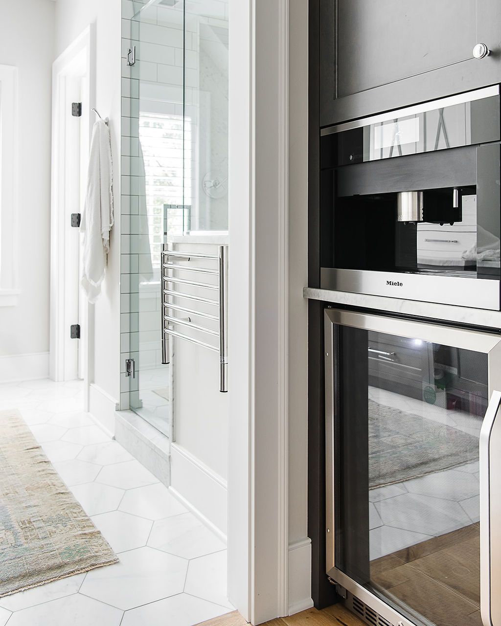 Bathroom with glass shower, built-in coffee machine, and small refrigerator. White walls, wood floor, and rug.
