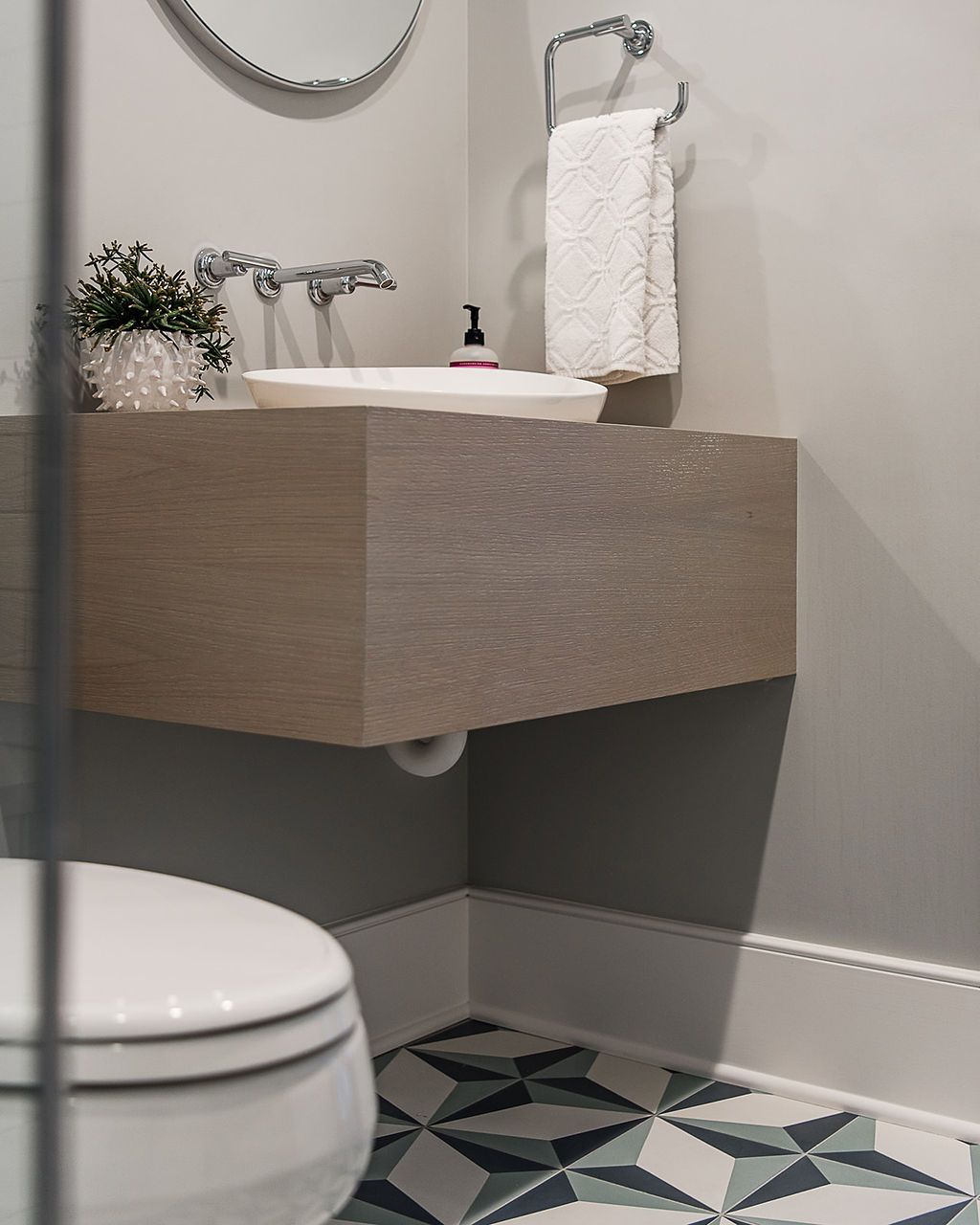 Floating wood vanity in a bathroom, with white sink, patterned floor, toilet, and towel rack.