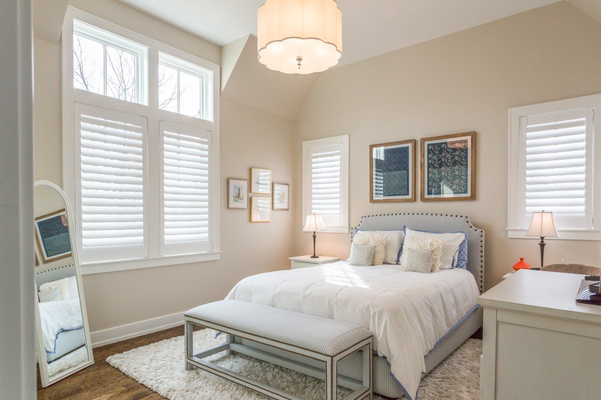 A bedroom with a bed , dresser , mirror and shutters.