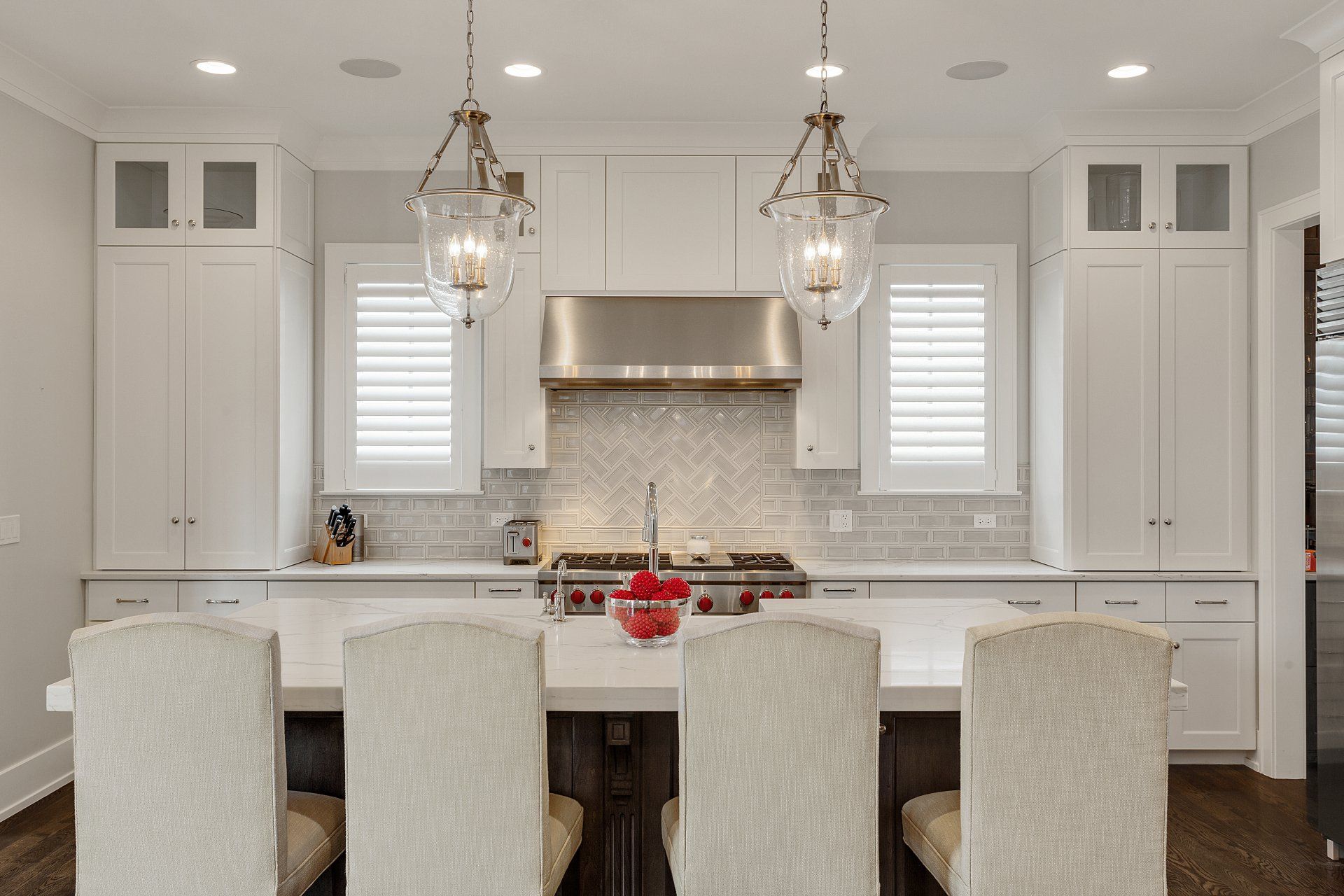 A kitchen with white cabinets , stainless steel appliances , a large island and dining chairs.