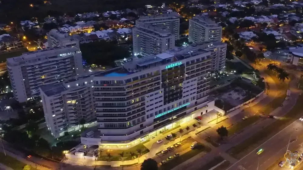 Vista aérea de un moderno complejo de apartamentos iluminado por la noche, junto a carreteras sinuosas y luces de la ciudad.