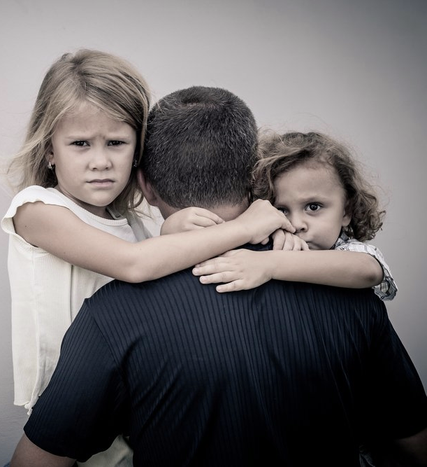 Two little girls hugging a man in a black shirt