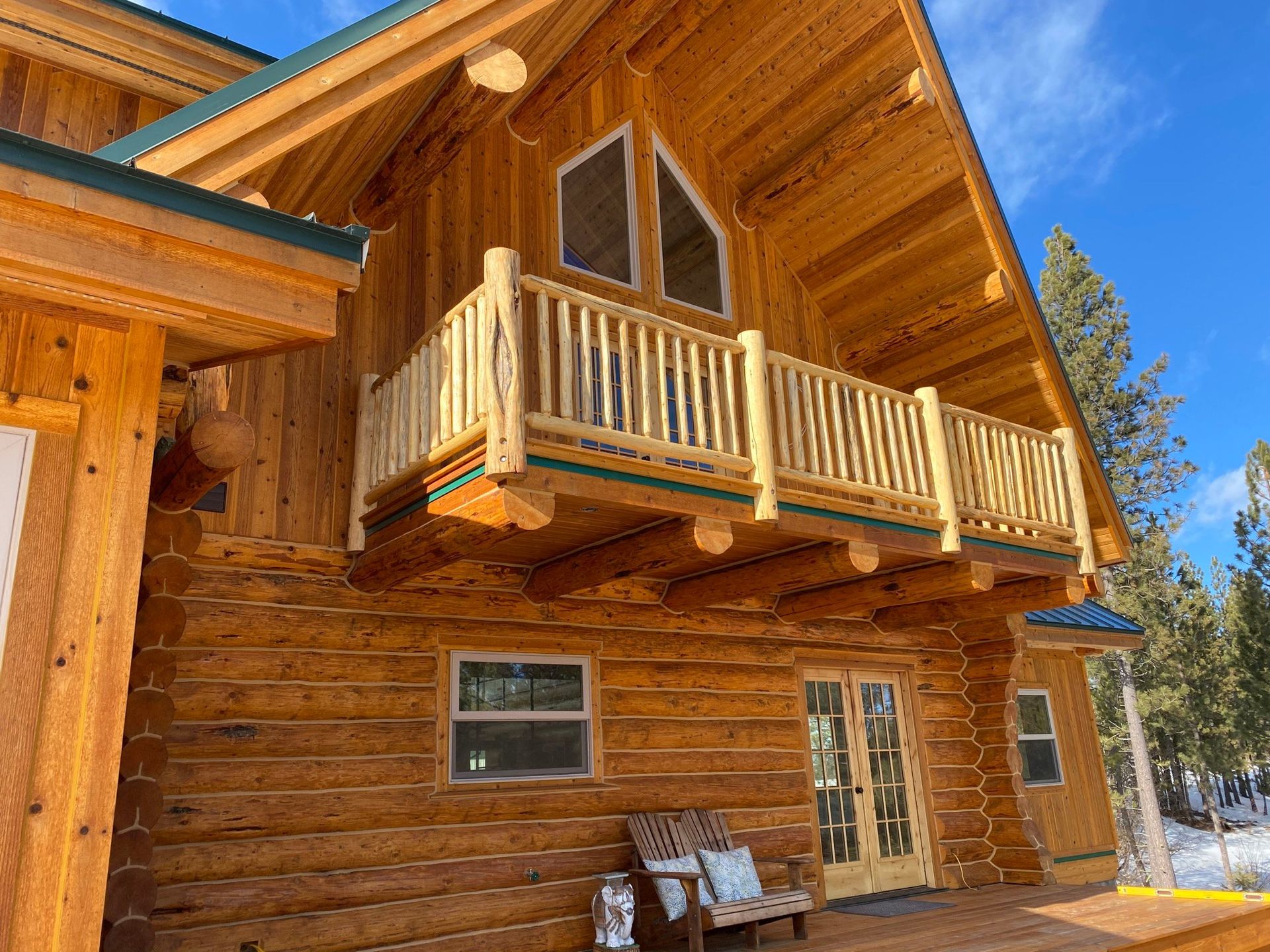 A log cabin with a balcony and a bench in front of it.