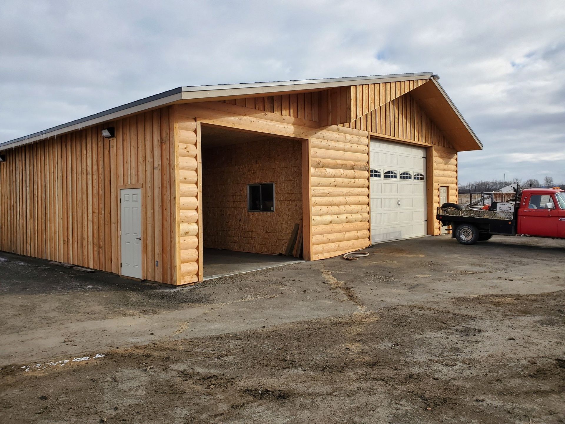 A red truck is parked in front of a wooden garage