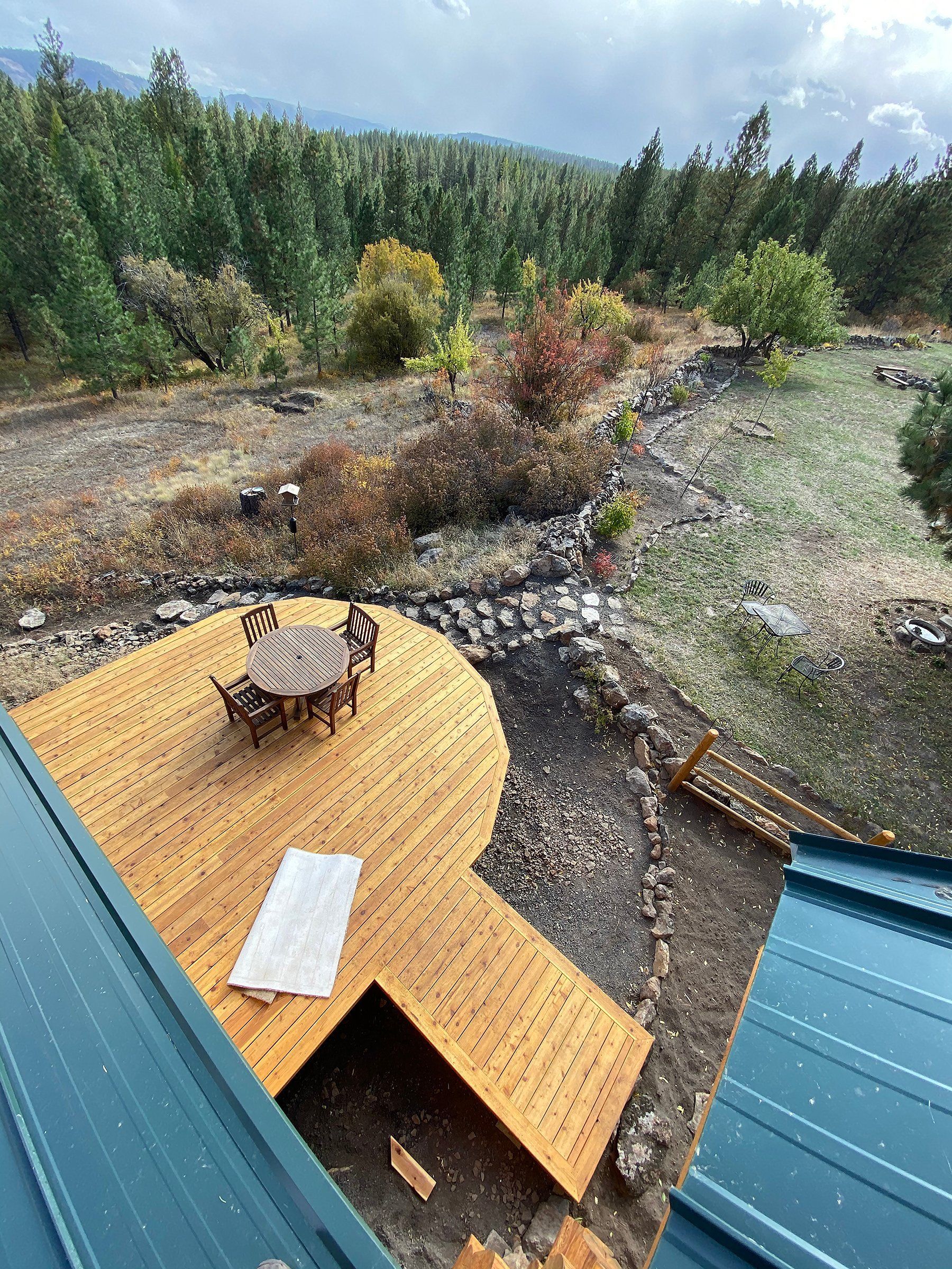 An aerial view of a wooden deck with a table and chairs in the middle of a forest.