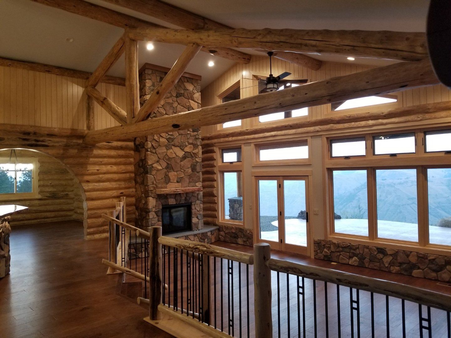 A large room in a log cabin with a fireplace and lots of windows.