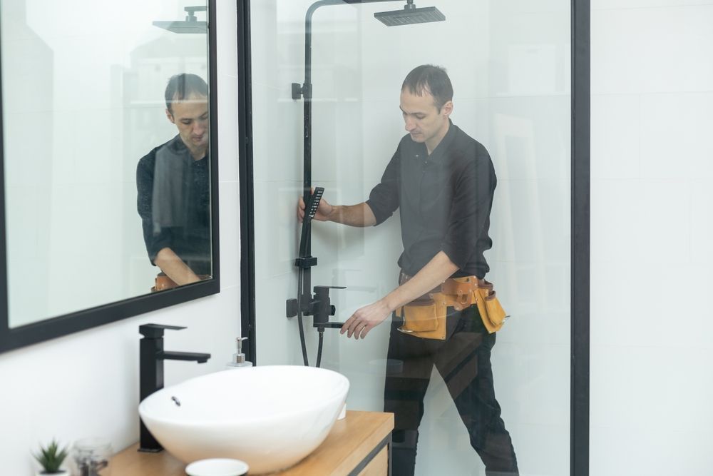 Man in black shirt installing shower fixture in a modern bathroom.
