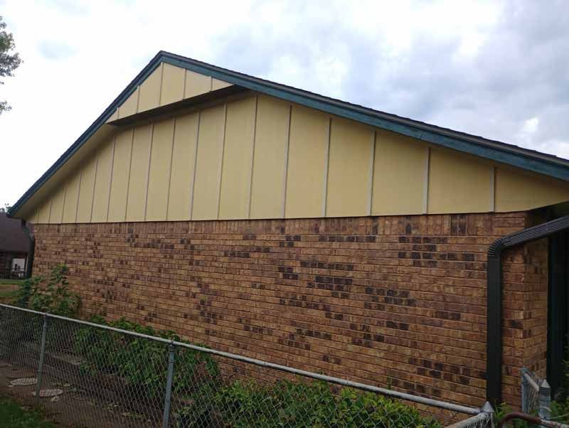 Brick building with yellow siding under a dark roof. A chain-link fence is in the foreground.