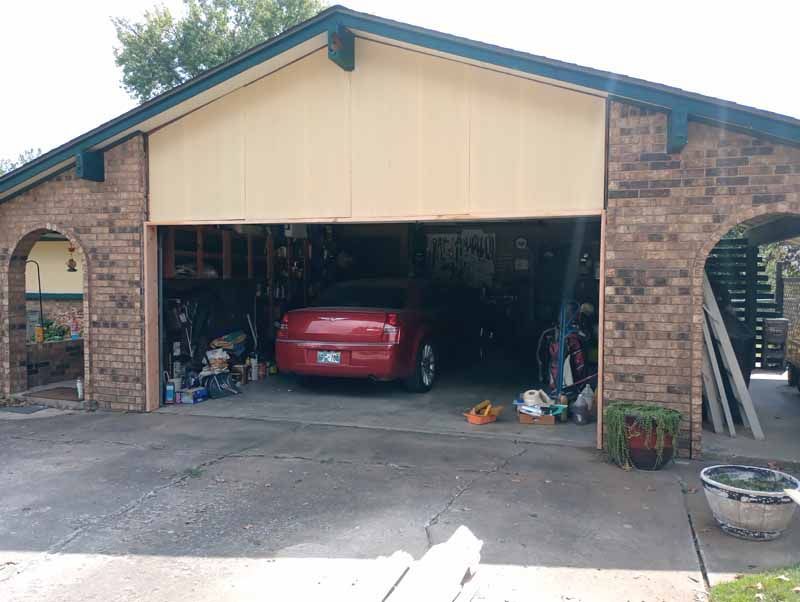 Brick garage with a red car inside, cluttered interior, beige overhang, and arched entryway.