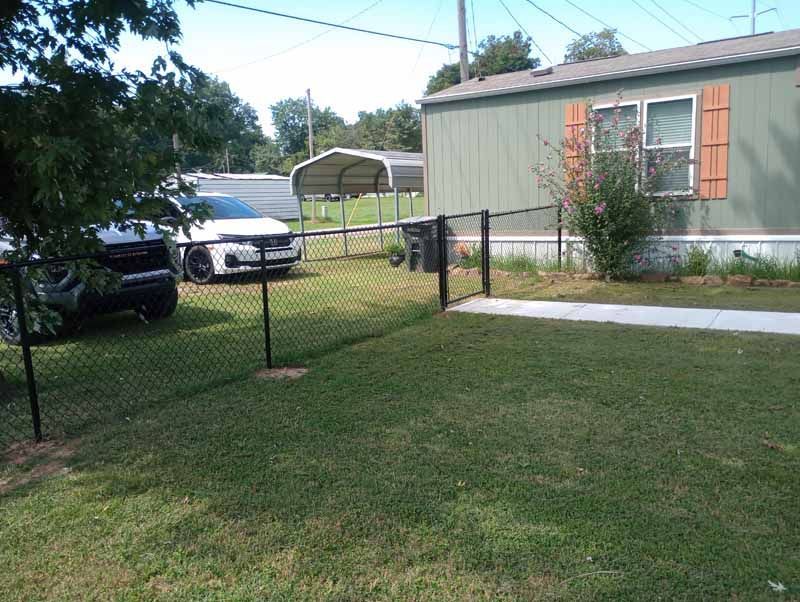Green lawn and black fence in front of a green house with a police car parked nearby.