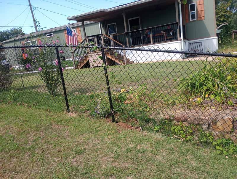 Black chain-link fence in front of a green house with a porch. American flag visible.