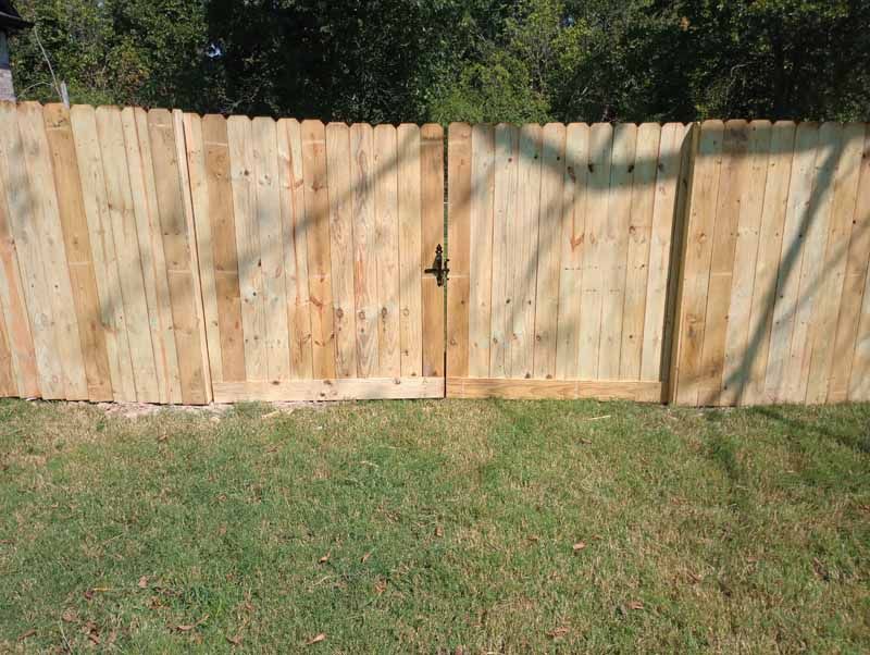 Wooden fence with gate in a grassy yard, trees in the background, latch on the gate.