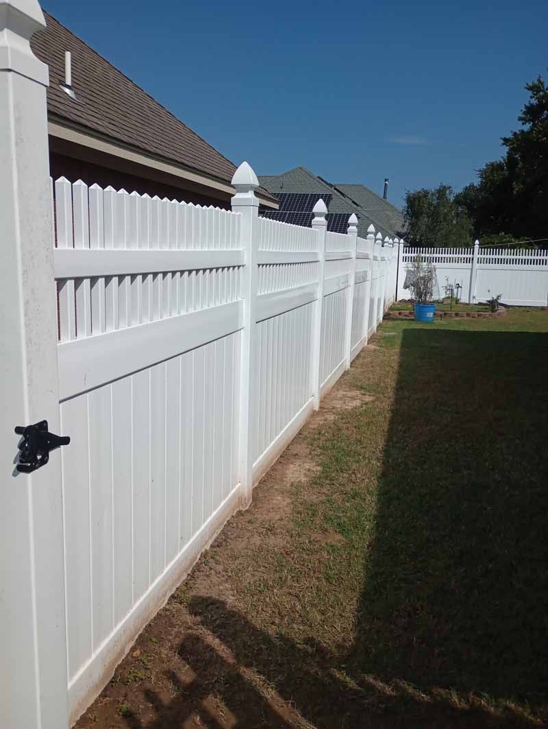 White vinyl fence along green grass and dry dirt path under blue sky.