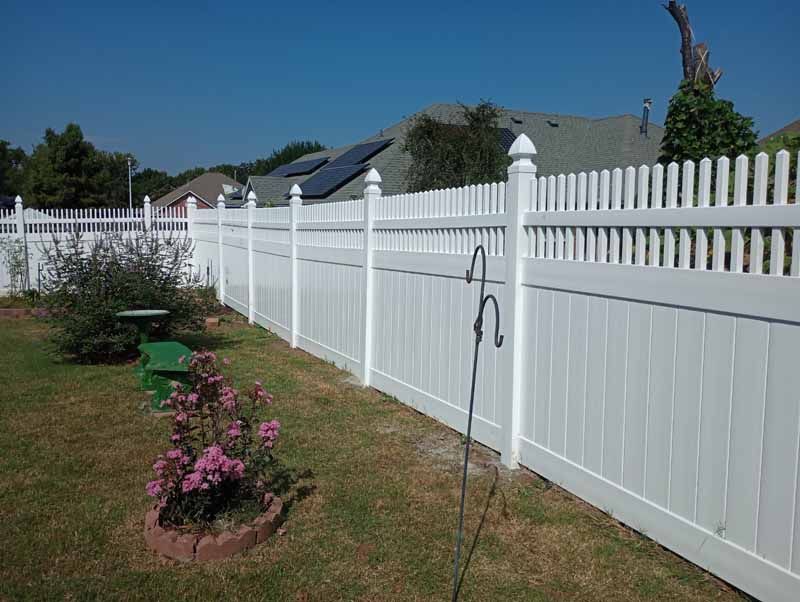 White picket fence in a grassy backyard on a sunny day.