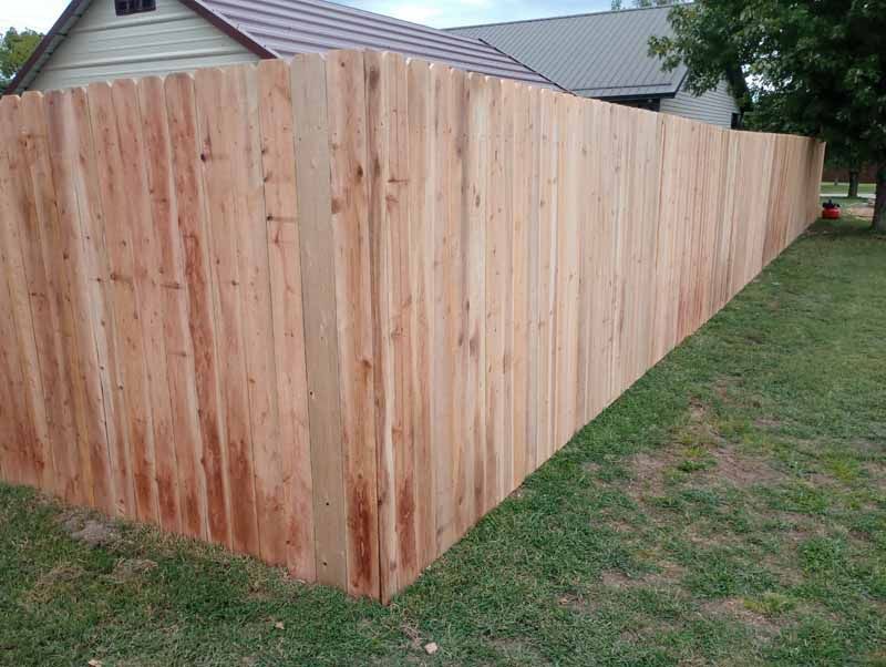 Wooden privacy fence enclosing a yard, green grass, and part of a house.