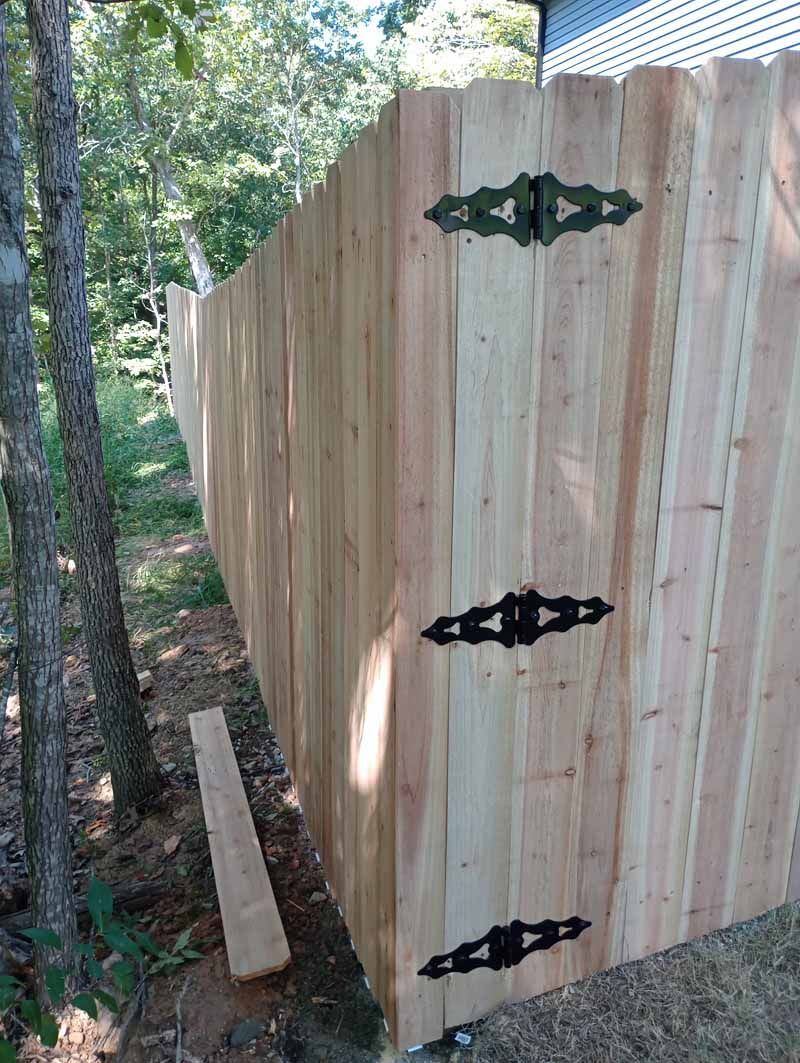 Wooden fence with black decorative hinges in a wooded area.