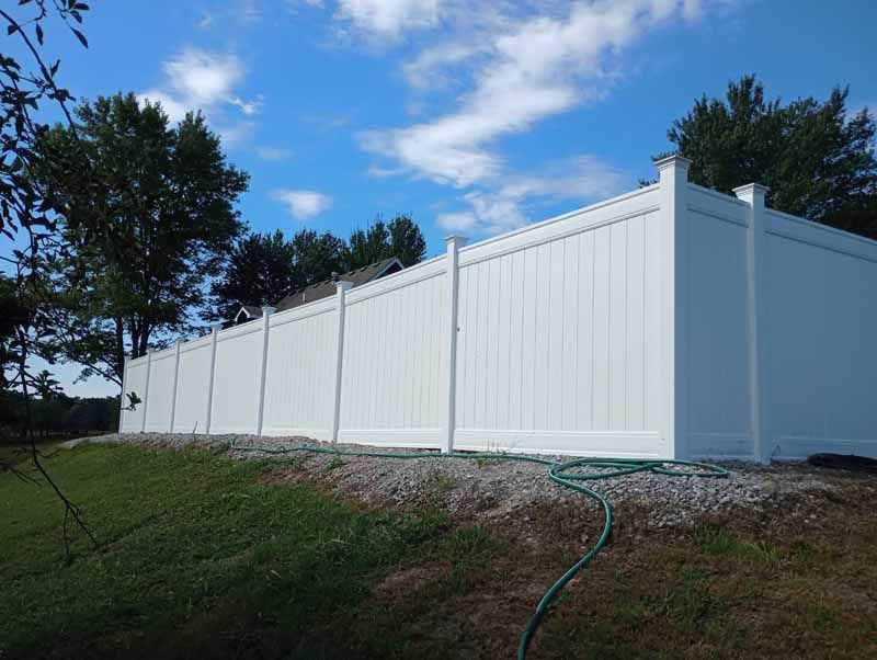 White vinyl fence along a grassy slope, blue sky with clouds in background.