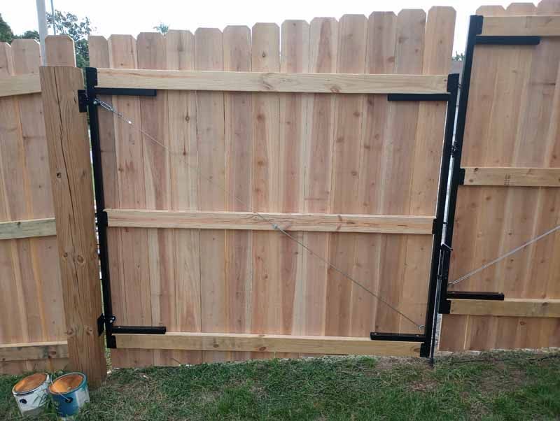Wooden fence gate with black metal hardware, closing against a wooden fence.