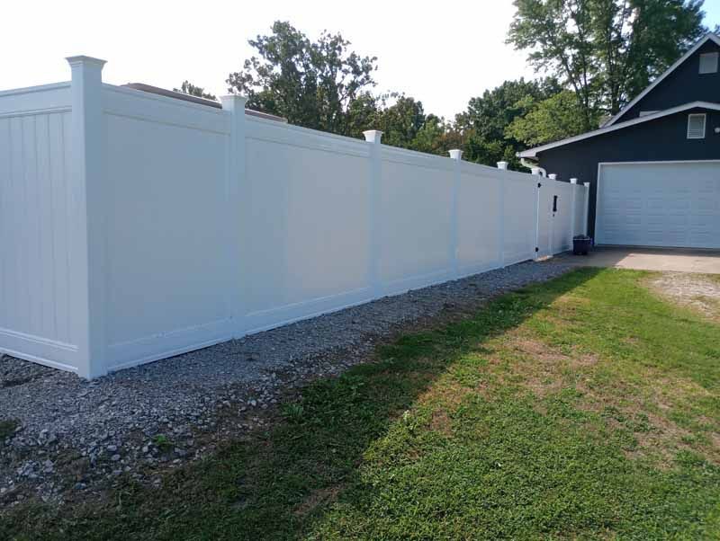 White vinyl privacy fence alongside a gravel path and grassy lawn next to a garage.
