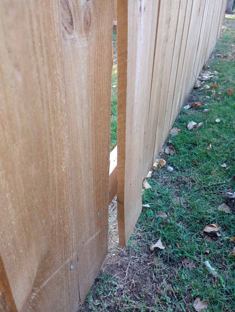 Wooden fence with a noticeable gap revealing green grass.