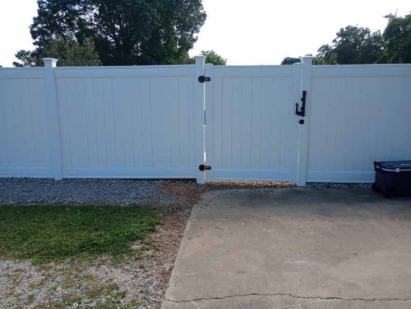 White vinyl fence with gate, set in a yard.  Gravel and concrete path in front.