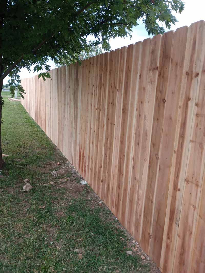 Wooden fence bordering a grassy yard, under a tree.