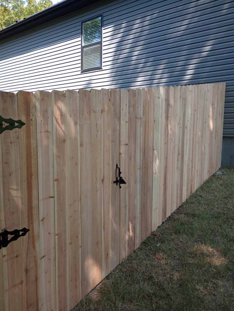 Wooden fence with a gate, attached to a gray house. Green grass in foreground.