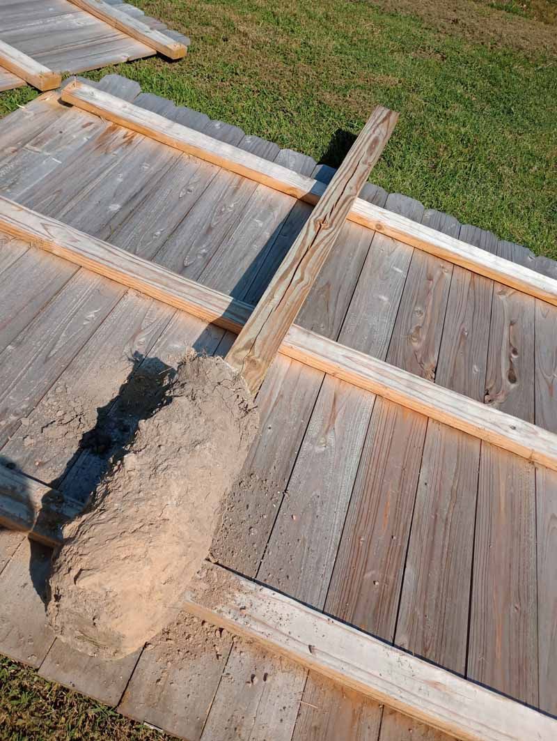 Wooden fence panels laid on grass, with a pile of dirt.