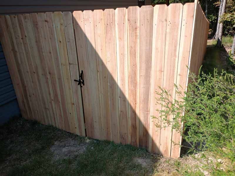 Wooden fence with gate; outdoors, grassy area, shadows cast by sunlight.