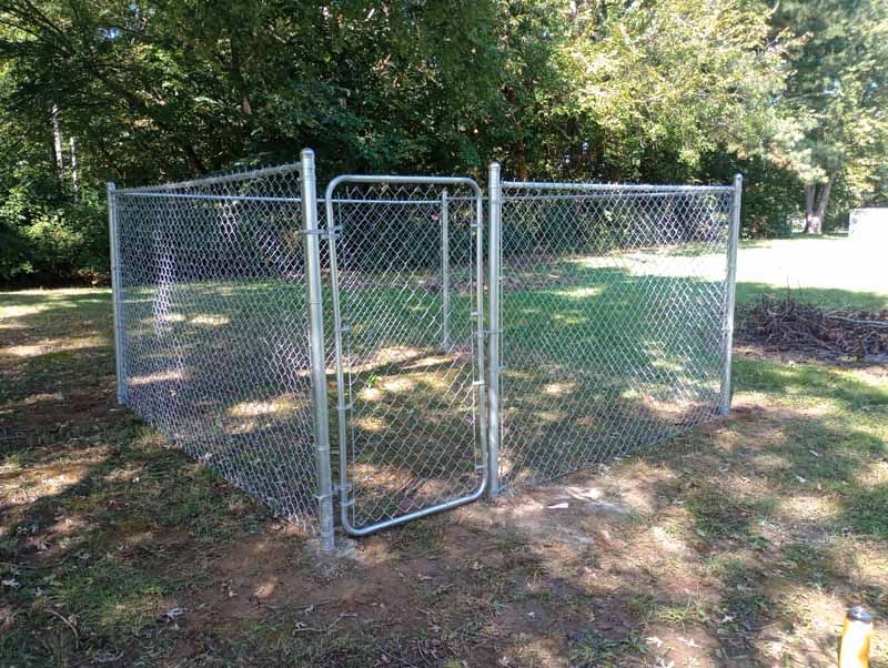 Chain-link fence with gate in a yard, surrounded by grass and trees.