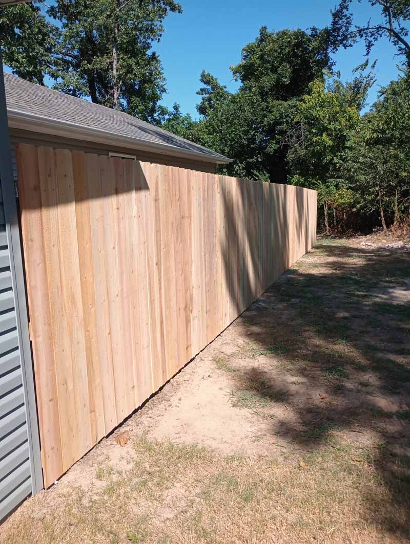 Wooden fence alongside a building under a blue sky, with trees in the background.