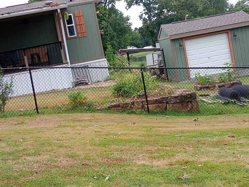 Green house and detached garage on a slight angle, with a black chain link fence in the yard.