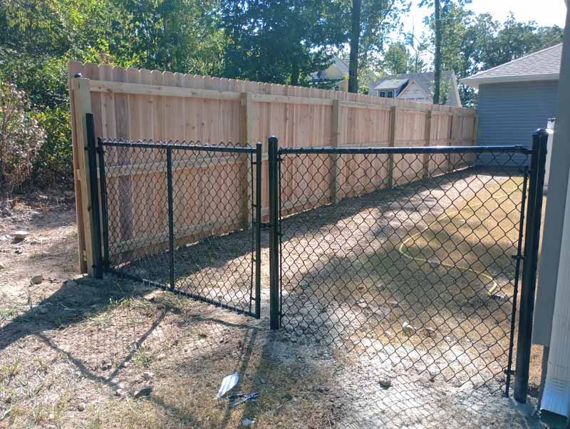 Black chain link gate and wooden fence in a yard.
