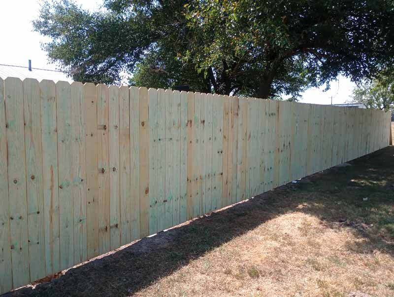 Wooden fence with scalloped top, built along grassy yard.