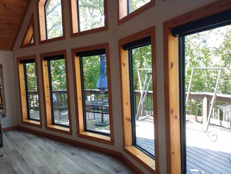 Interior view of room with large windows, wooden frames, and outdoor deck visible.