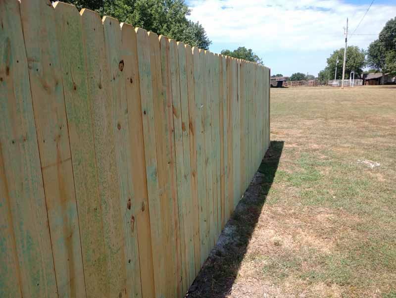 Wooden fence bordering a grassy field under a bright, sunny sky.