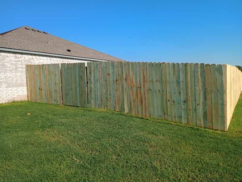 Wooden fence in a yard next to a house with a clear blue sky.