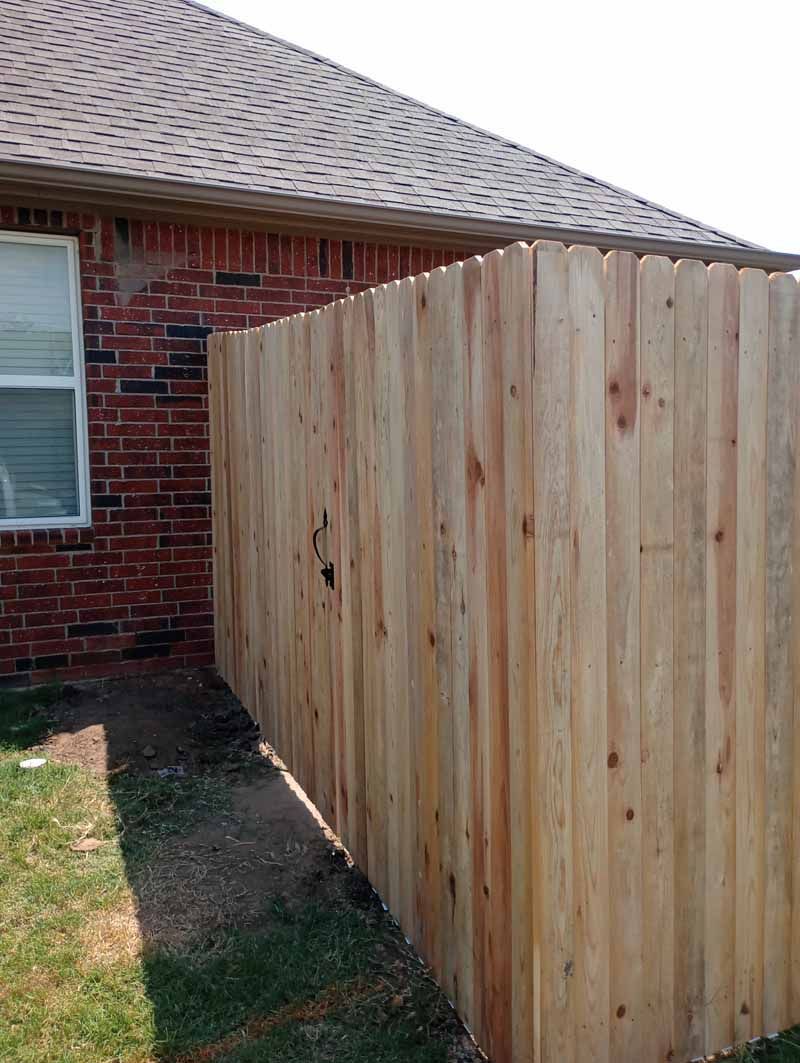 Wooden fence alongside a brick house with a window, set on grass.