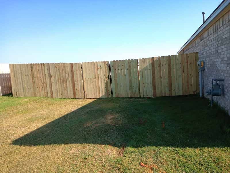 Wooden fence in backyard, next to a brick building.