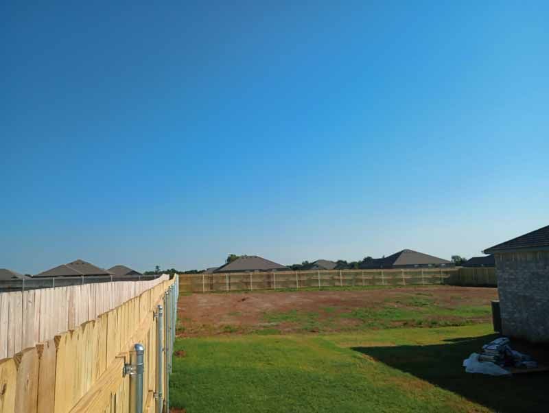 Wooden fence framing a yard with a clear blue sky, other houses visible in the distance.