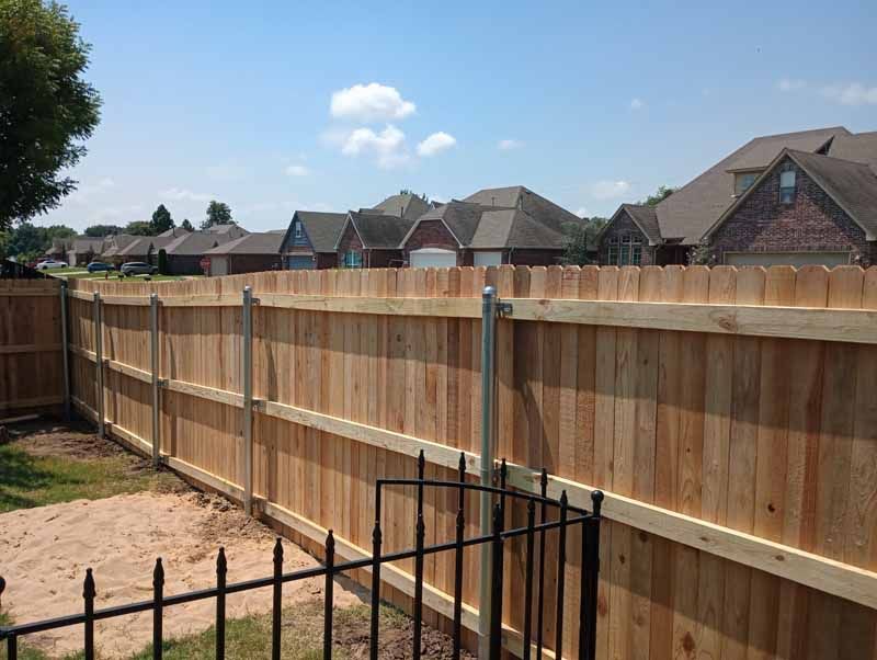 Wooden fence in a residential backyard, separating it from other houses under a blue sky.