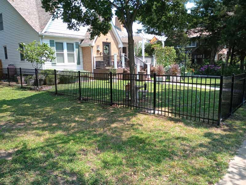 Black metal fence enclosing a front yard with trees and houses.