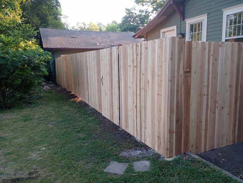 Wooden fence alongside a green house and garage, with grass in the foreground.