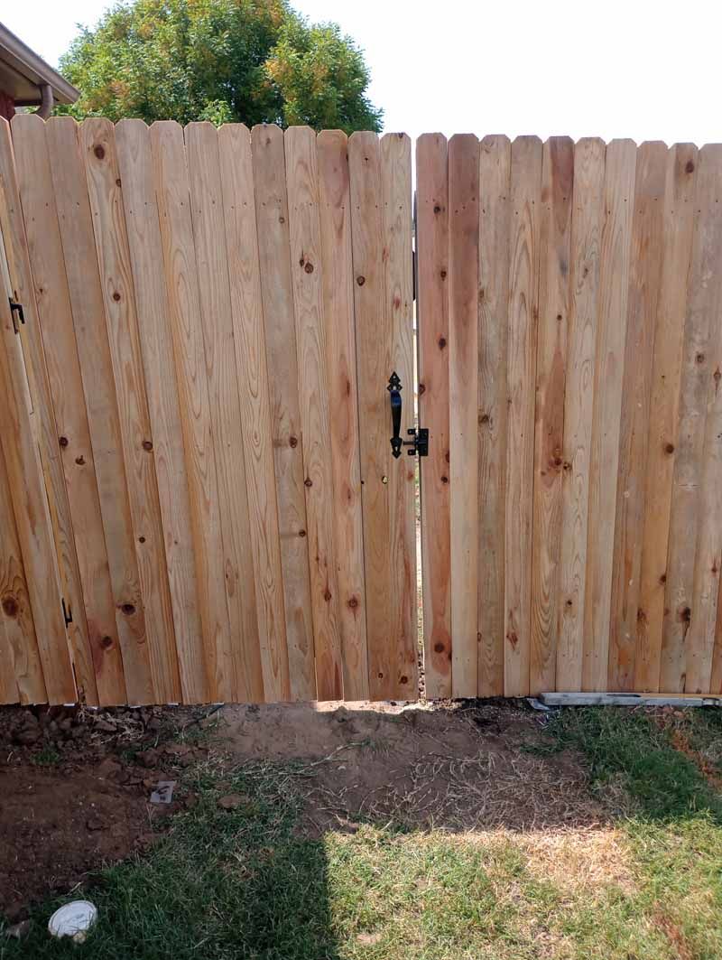 Wooden fence with gate, set in grass, against a background of trees.