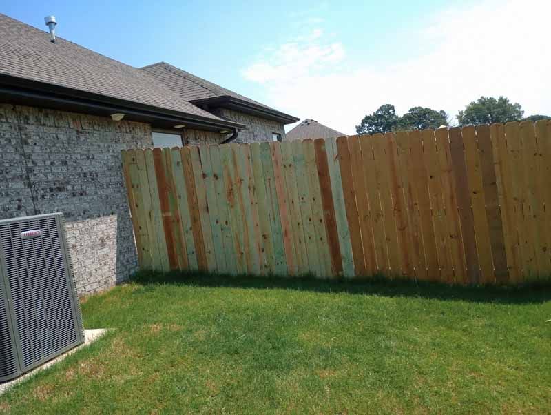 Backyard with brick house, wooden fence, grass, and an air conditioner unit on a sunny day.