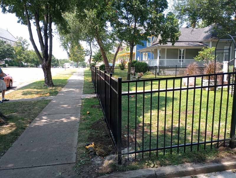 Black metal fence along a sidewalk in front of a house.