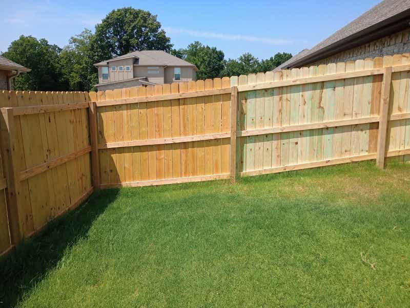 Wooden fence encloses a green lawn in a backyard, with a house visible in the background.