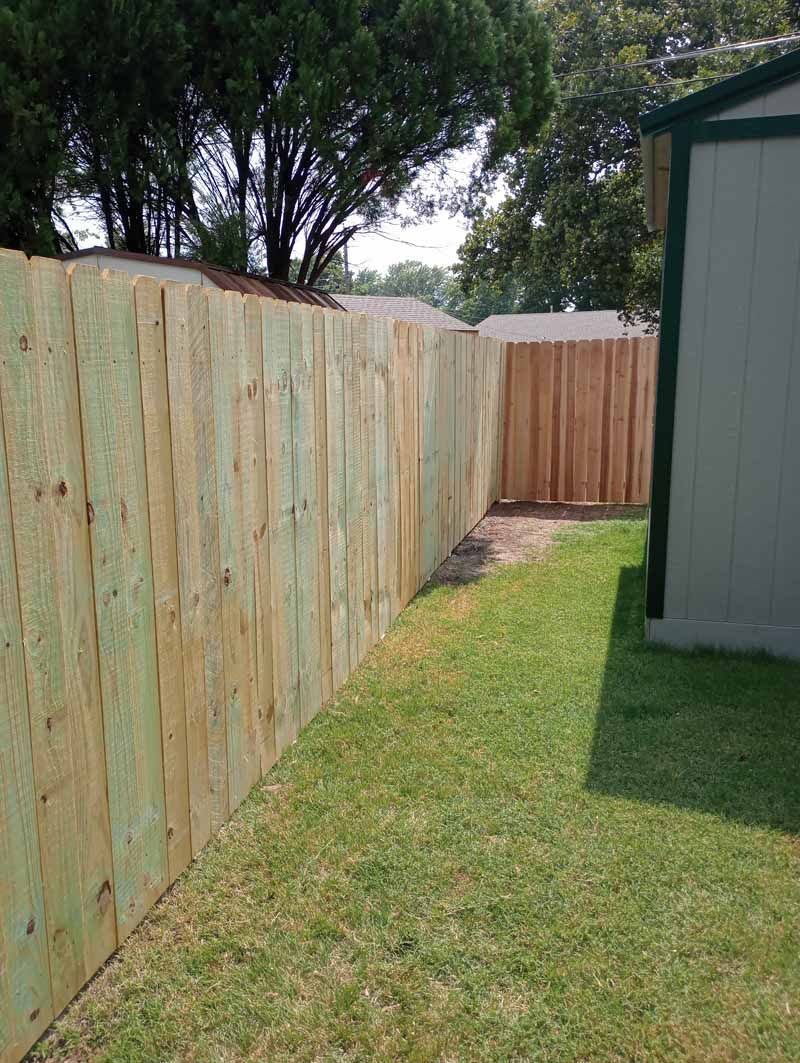 Wooden fence along green grass next to a light-colored shed.